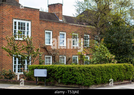 Maison en brique de deux étages avec des fenêtres blanches. Quartier calme dans le centre de Londres, le jardin avant de haies, printemps, arbres en fleurs. Banque D'Images