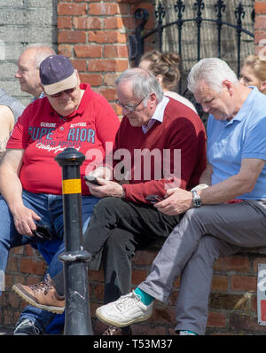 Deux vieux amis étaient assis ensemble sur un mur en se concentrant sur leurs téléphones mobiles. Banque D'Images