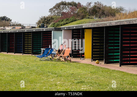 Des chaises en bois en face de cabines de plage au soleil Banque D'Images
