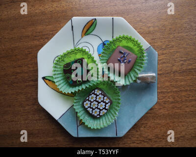 Trois bonbons au chocolat fantaisie en vert wrappers sur un plat en porcelaine sur une table en bois. Banque D'Images