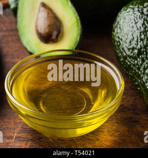 Bol avec de l'huile et l'avocat frais sur table en bois. Banque D'Images