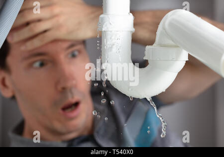 Jeune homme choqué à la fuite du tuyau de l'évier de cuisine en Banque D'Images