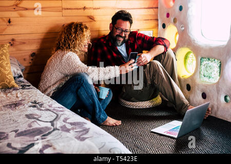 Couple adultes bénéficiant de la technologie à la maison ou à l'hôtel voyager avec un téléphone mobile à écran de l'appareil et à l'aide d'un ordinateur portable connecté à internet sur la flo Banque D'Images