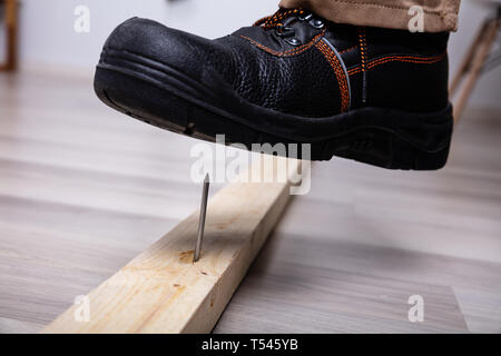 Close-up of Man's Foot Enjambant Il Nail inséré dans planche en bois Banque D'Images