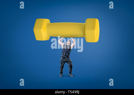 Strong muscular young man holding un gros haltère jaune sur fond bleu Banque D'Images