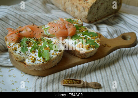 Sandwichs sur deux morceaux de pain de seigle avec du fromage à la crème, la roquette, les graines de moutarde et de saumon sur la planche de bois. Concept de la saine alimentation à la mode. Delici Banque D'Images