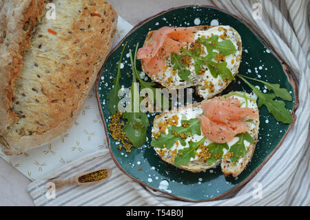 Petit-déjeuner sain de deux sandwiches au saumon au fromage à la crème, la roquette sur la plaque en céramique vert à pois blancs. Cuillère en bois avec les graines de moutarde. Hea Banque D'Images