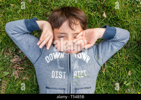 Un jeune garçon se couche sur l'herbe, et s'étend. Banque D'Images