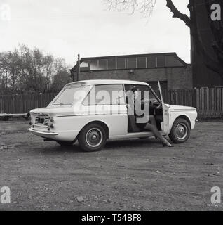 1967, historiques, jeune femme portant une jupe de laine cardigan et assis dans le siège du conducteur d'un rayon de soleil, les deux voitures de sport-porte sports version de la célèbre petite voiture, l'HIllman Imp. L'Hillman Imp est une petite voiture fabriquée par Rootes Group et son successeur Chrysler Europe de 1963 jusqu'en 1976 a été le concurrent dans la catégorie des petites voitures à la Mini. Banque D'Images