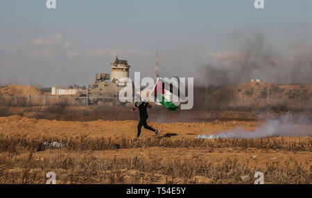 Gaza, Khan Younis, Palestine. Apr 19, 2019. Un manifestant palestinien vu courir tout en tenant un drapeau au milieu de la fumée des gaz lacrymogènes pendant la manifestation.Palestiniens entrent en conflit avec les forces israéliennes au cours d'une manifestation appelant à la levée du blocus israélien de Gaza et exigeant pour le droit de retourner dans leur patrie, à l'Israel-Gaza clôture frontalière dans le sud de la bande de Gaza. Credit : Yousef Masoud SOPA/Images/ZUMA/Alamy Fil Live News Banque D'Images