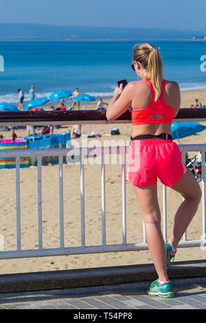 Bournemouth, Dorset, UK. 21 avr 2019. Météo France : la canicule se poursuit avec le temps ensoleillé et chaud, en tant que chef de la plage au bord de la mer pour profiter de la chaleur et du soleil à plages de Bournemouth pour les vacances de Pâques - le milieu de la matinée et les plages sont déjà obtenir paniers, comme sunseekers arriver tôt pour obtenir leur espace. Young woman standing on pier looking at mobile phone. Credit : Carolyn Jenkins/Alamy Live News Banque D'Images