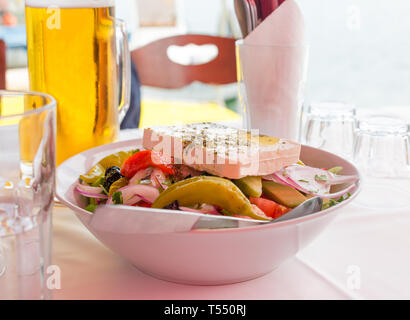 Bol de salade grecque avec fromage feta, poivrons, tomates, concombres, olives et oignons rouges. Beer mug et verres vides sur la table Banque D'Images