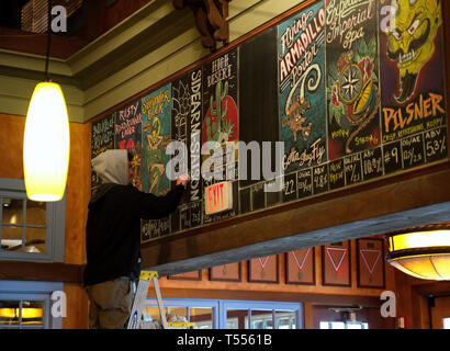 Fairfax, VA USA. Mar 2019. Un jeune homme sur l'échelle d'appliquer ses compétences artistiques pour illustrer un menu de boissons alcoolisées sur un restaurant au tableau. Banque D'Images