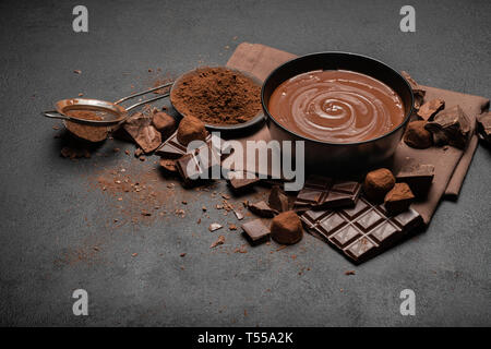 Bol en céramique de crème au chocolat ou le chocolat fondu et les morceaux de chocolat isolé sur fond de béton foncé Banque D'Images