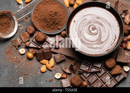 Bol en céramique de crème au chocolat ou le chocolat fondu, les noix et les morceaux de chocolat sur fond de béton foncé Banque D'Images