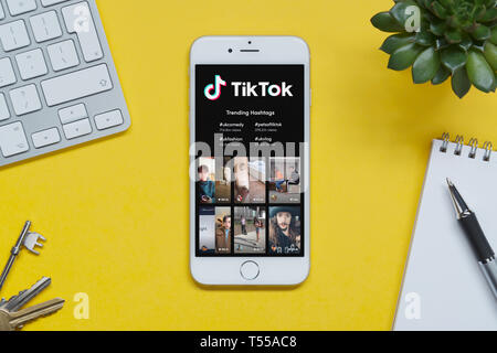Un iPhone montrant l'Tik Tok site repose sur un fond jaune table avec un clavier, les touches, le bloc-notes et des plantes (usage éditorial uniquement). Banque D'Images