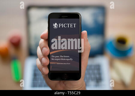 Un homme se penche sur son iPhone qui affiche le logo Pictet (usage éditorial uniquement). Banque D'Images