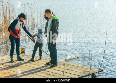 Père et Mère avec enfant Garçon jouant avec de l'eau banc près de Riverside. Banque D'Images