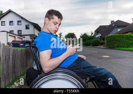 Garçon handicapé avec le smartphone en attente de l'autobus scolaire Banque D'Images