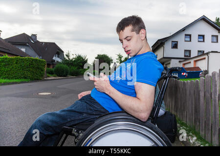 Garçon handicapé avec le smartphone en attente de l'autobus scolaire Banque D'Images