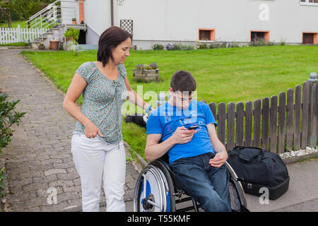 Mère et fils handicapé en attente de l'autobus scolaire Banque D'Images