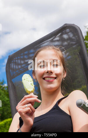 Teenage girl eating les sucettes glacées dans un transat, dans un jardin Banque D'Images