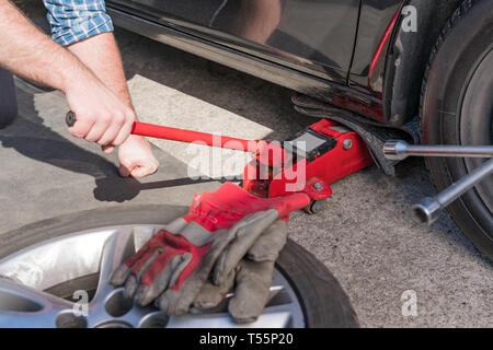 Homme de soulever voiture sur une allée. Changement de pneus saisonniers ou service concept abstrait. Banque D'Images