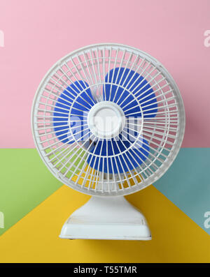 Ventilateur en plastique blanc avec des volets bleus sur un fond pastel multicolores. Vue d'en haut. Banque D'Images