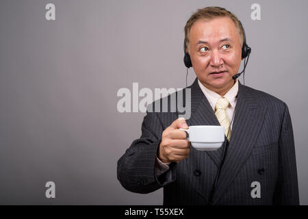 Portrait of mature Asian businessman contre l'arrière-plan gris Banque D'Images