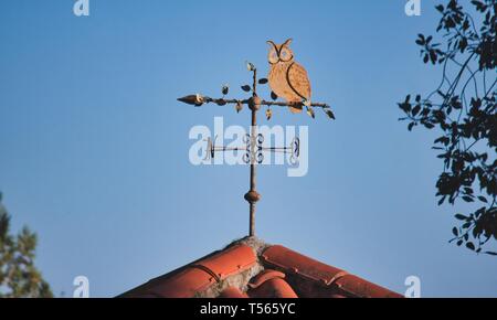 Girouette métallique en forme d'un hibou sur le dessus d'un toit de tuiles en terre cuite sur un fond de ciel bleu Banque D'Images