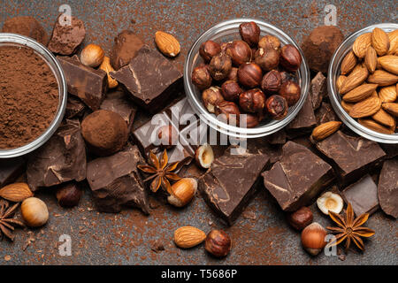 Des tas de morceaux de chocolat et les noix brisées sur fond de béton foncé Banque D'Images