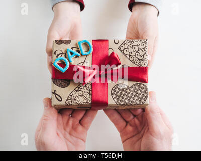 Les mains de l'enfant et l'adulte man's hands, superbe boîte cadeau, ruban et enrobée de cookies sur un fond de bois, blanc. Vue de dessus, close-up. La préparation pour le th Banque D'Images