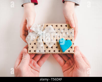 Les mains de l'enfant et l'adulte man's hands, superbe boîte cadeau, ruban et enrobée de cookies sur un fond de bois, blanc. Vue de dessus, close-up. La préparation pour le th Banque D'Images