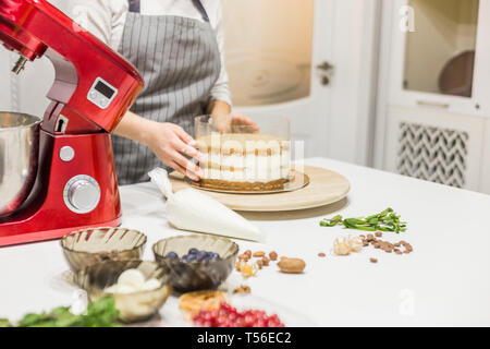 Jeune femme pâtissier bat la crème dans un bol en métal rouge dans un mélangeur électrique. Le concept de pâtisserie maison, la cuisine. Banque D'Images