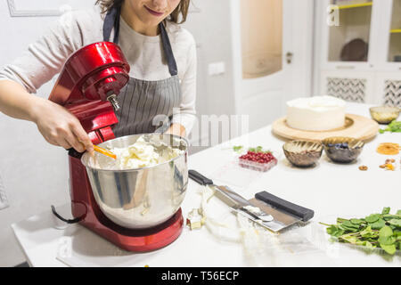 Jeune femme pâtissier bat la crème dans un bol en métal rouge dans un mélangeur électrique. Le concept de pâtisserie maison, la cuisine. Banque D'Images