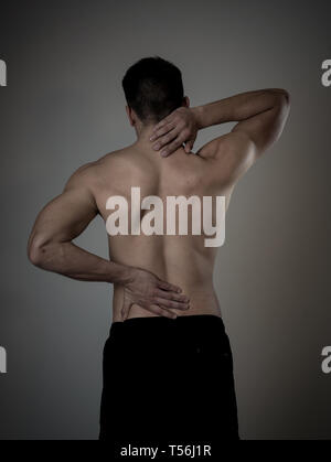 Jeune homme remise en forme musculaire touchant et saisissant son cou et le bas du dos douleurs cervicales souffrance isolé sur fond neutre. Dans le sport et d'entraînement Banque D'Images