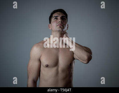 Jeune homme fit musculaire touchant et saisissant le cou et le haut du dos souffrant de douleur cervicale après entraînement. Isolé sur fond neutre. Dans le sport après accidents du travail Banque D'Images