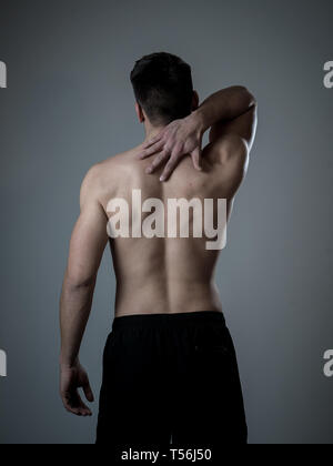 Jeune homme fit musculaire touchant et saisissant le cou et le haut du dos souffrant de douleur cervicale après entraînement. Isolé sur fond neutre. Dans le sport après accidents du travail Banque D'Images