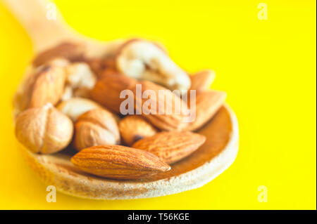 Mélange de noix dans une cuillère en bois sur fond jaune. Le petit-déjeuner, collation biologiques sains, naturels ingrédients alimentaires. Banque D'Images