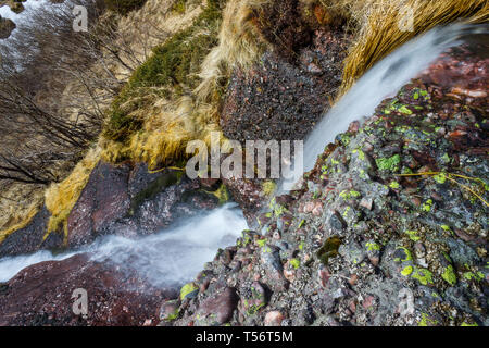 Cascade de montagne puissante sur la falaise rouge couverts par de petites roches et vif, vert mousse Banque D'Images