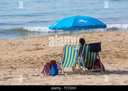 Bournemouth, Dorset, UK. 22 avr, 2019. Météo France : après un démarrage par temps brumeux la glorieuse continue avec eau chaude et ensoleillée, en tant que chef de la plage au bord de la mer pour profiter de la chaleur et du soleil à plages de Bournemouth le lundi de Pâques avant le temps change et le retour au travail. Deux chaises longues avec parasol bleu avec l'homme assis dans une chaise longue.Credit : Carolyn Jenkins/Alamy Live News Banque D'Images