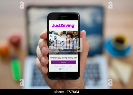 Un homme se penche sur son iPhone qui affiche le logo JustGiving (usage éditorial uniquement). Banque D'Images