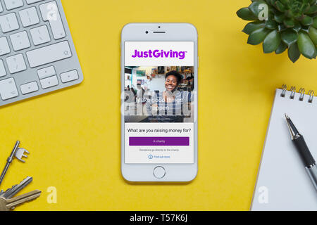 Un iPhone montrant le site JustGiving repose sur un fond jaune table avec un clavier, les touches, le bloc-notes et des plantes (usage éditorial uniquement). Banque D'Images