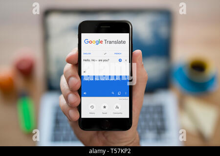 Un homme se penche sur son iPhone qui affiche le logo Google Translate (usage éditorial uniquement). Banque D'Images