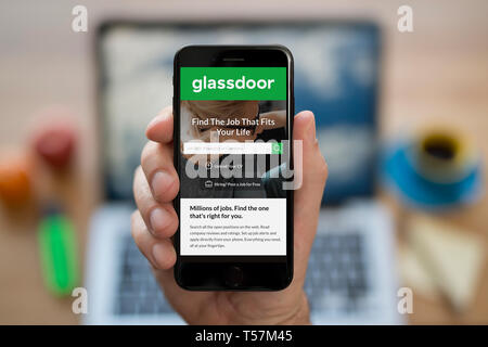 Un homme se penche sur son iPhone qui affiche le logo Glassdoor (usage éditorial uniquement). Banque D'Images