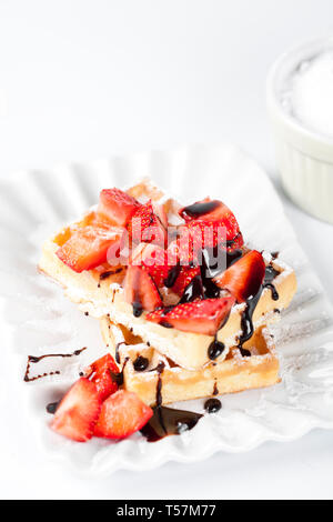 Belgique waffers avec du sucre en poudre, des fraises et du chocolat sur une plaque en céramique sur le tableau blanc. Des wafers. Banque D'Images