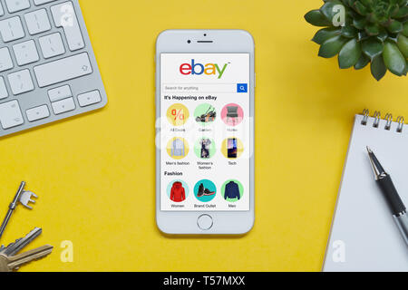 Un iPhone montrant le site web d'ebay repose sur un fond jaune table avec un clavier, les touches, le bloc-notes et des plantes (usage éditorial uniquement). Banque D'Images