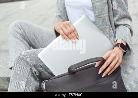 Jeune femme assise sur la ville street mettre portable en cas close-up Banque D'Images
