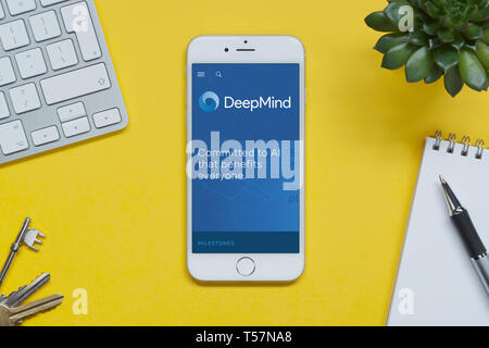 Un iPhone montrant le site web DeepMind repose sur un fond jaune table avec un clavier, les touches, le bloc-notes et des plantes (usage éditorial uniquement). Banque D'Images
