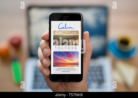 Un homme se penche sur son iPhone qui affiche le logo de l'app calme (usage éditorial uniquement). Banque D'Images